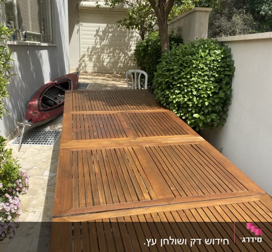 שולחן עץ ארוך בגינה ליד שיחים ירוקים